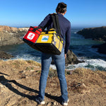 A woman with a yellow and red KitBrix transition bag, ready for adventure, traveling from the sea to the mountains.